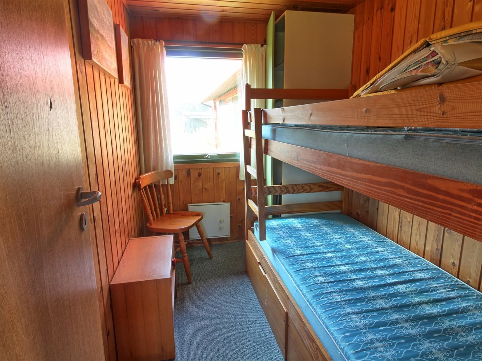 A bunk bed room with a wooden chair and a small table.