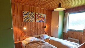 Et rum med træpaneler, en seng, to væglamper og et vindue med gardiner.