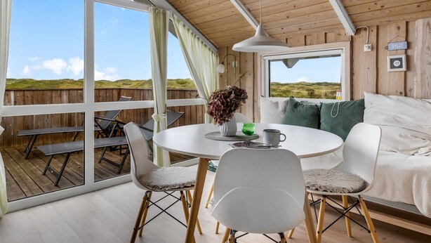 A cozy room with a large sliding glass door leading to an outdoor deck, a round dining table with chairs, and a bed with green pillows. - "Betti" - 300m from the sea by Interhome (Rømø)