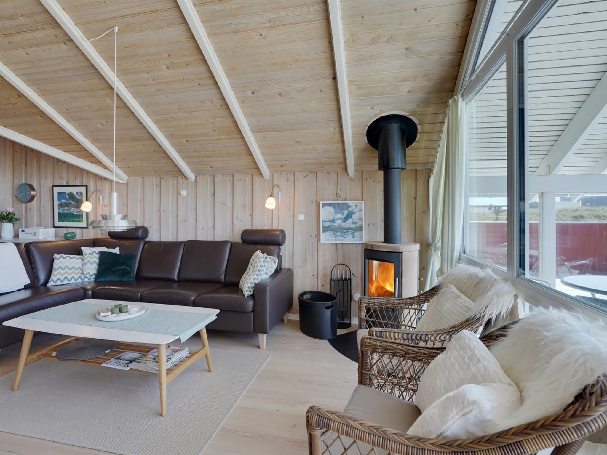A cozy living room with a wooden ceiling, a fireplace, a sofa, a coffee table, and wicker furniture.