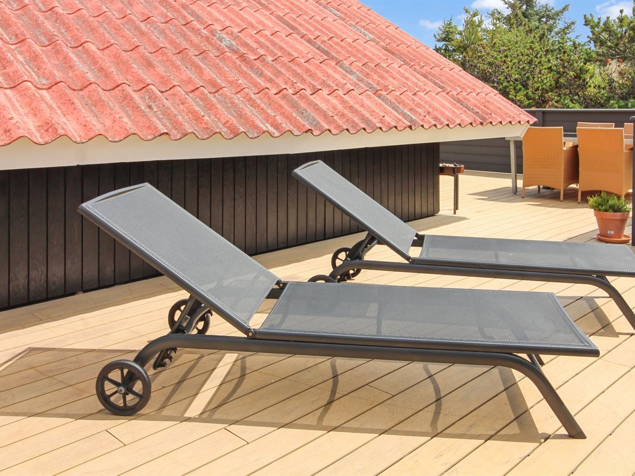 Two sun loungers on a wooden deck with a red-tiled roof in the background.