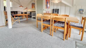 Un loft espacioso con techos altos, vigas de madera a la vista, una zona de comedor con mesa y sillas de madera, un sofá y una pequeña cocina.