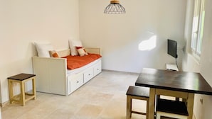 A room with a bed, a table, and a chair. There is a small stool and a TV on the wall.