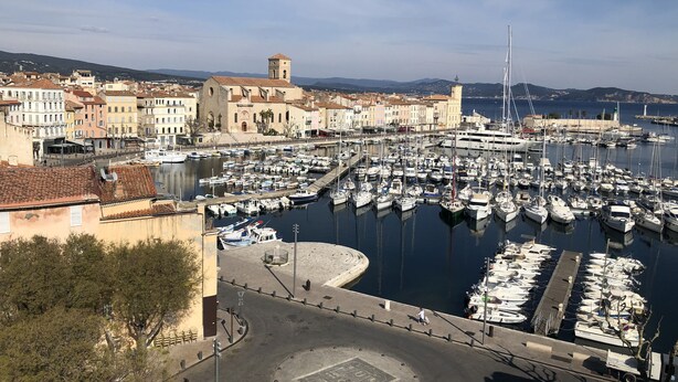 A marina with numerous boats docked, surrounded by historic buildings and a prominent tower.