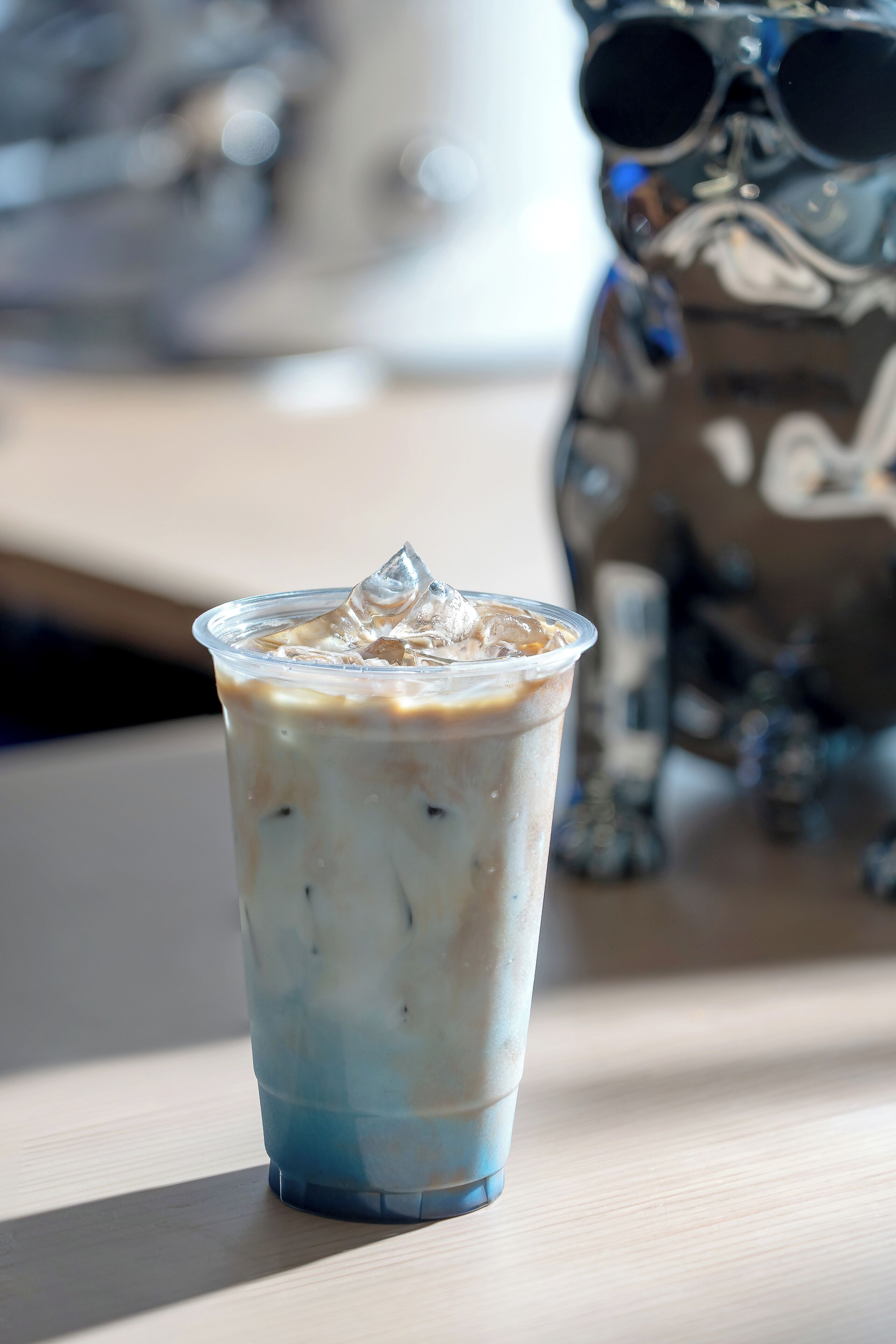 A clear plastic cup with a blue bottom and a white top, filled with a beverage and ice cubes, placed on a wooden surface.
