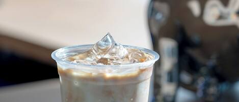 A clear plastic cup with a blue bottom and a white top, filled with a beverage and ice cubes, placed on a wooden surface.