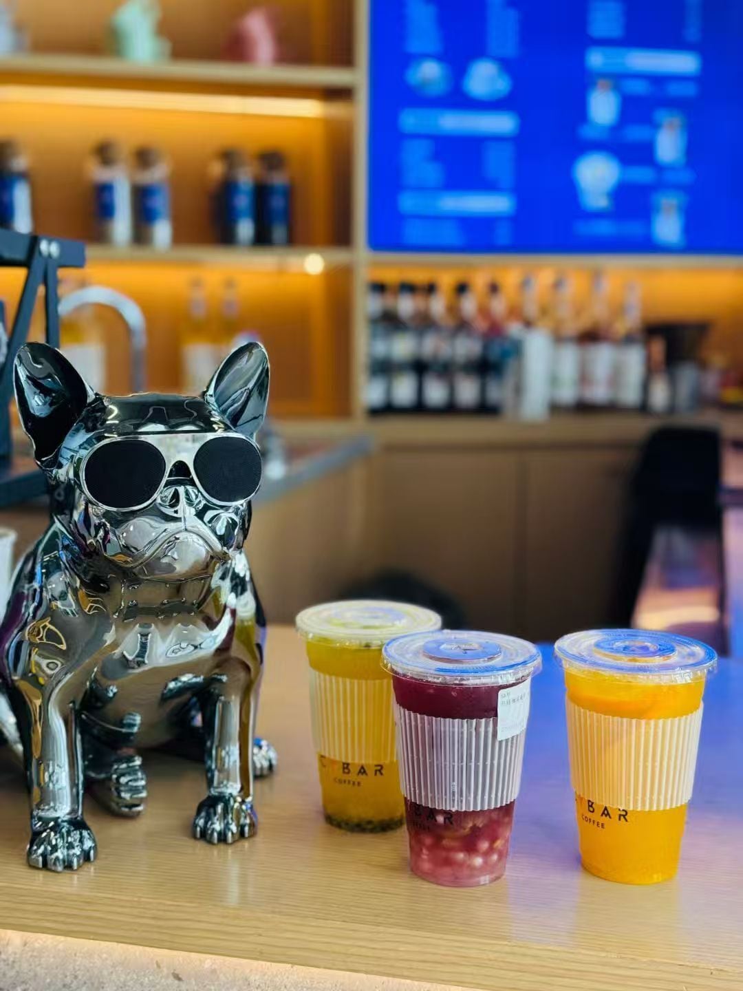 Eine Bar mit einer dekorativen Hundfigur, einem blauen Bildschirm mit Text und drei Kaffeetassen.