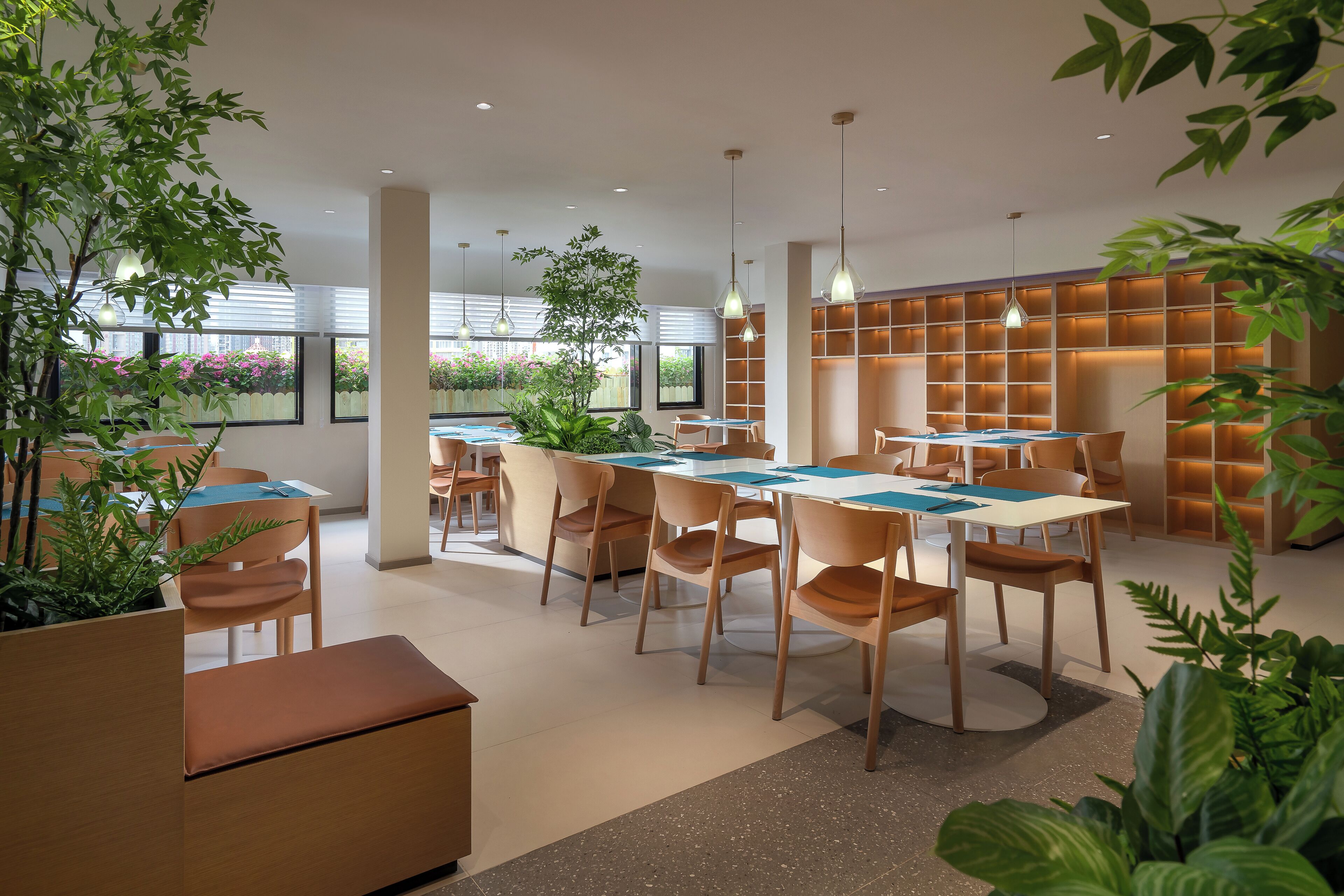 A modern dining area with wooden tables and chairs, potted plants, and pendant lighting.