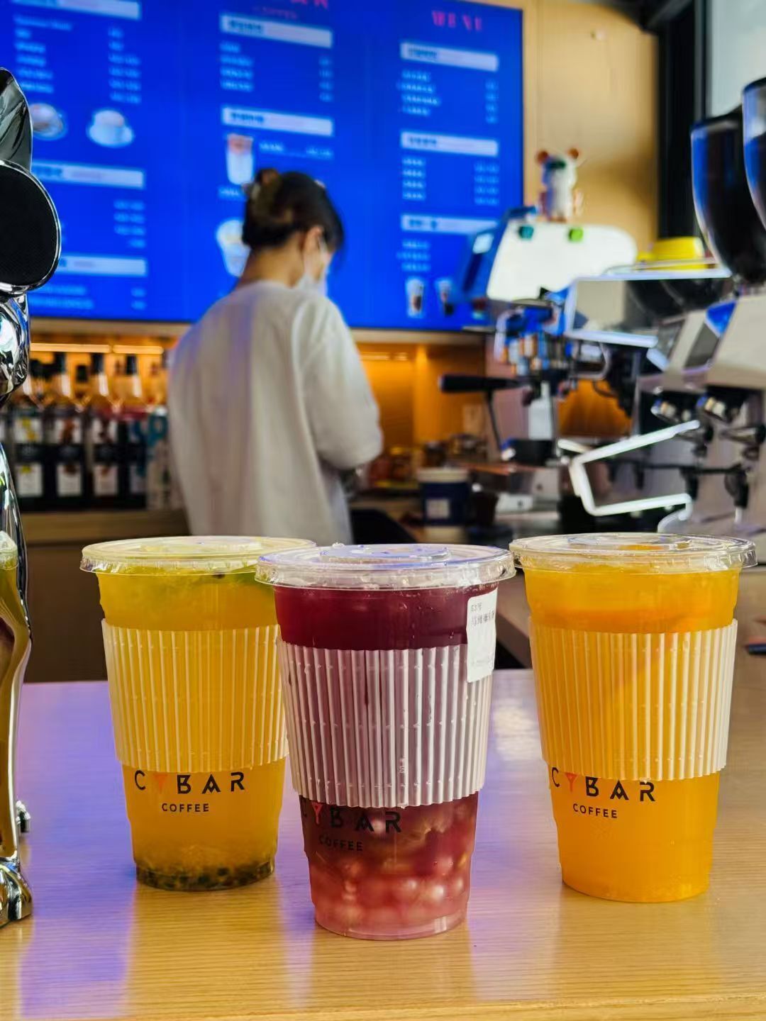 Three CYBAR coffee cups on a counter with a menu board in the background.