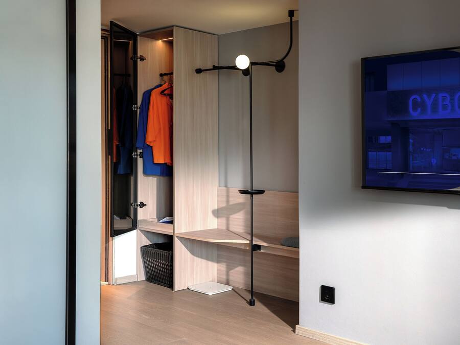 Een moderne kamer met een kledingkast, een aan de muur bevestigde televisie waarop 'CYBO' staat en een vloerlamp.