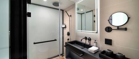 A modern bathroom with a glass shower enclosure, a large mirror, and a black vanity with a sink.