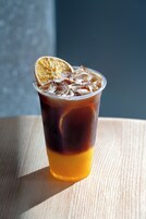 A clear glass of iced tea with a slice of orange on the rim, placed on a wooden surface.