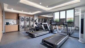 Un gimnasio moderno con cintas de correr, bicicletas estáticas y un amplio ventanal con vistas a zonas verdes.