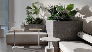 Un interior moderno con un sofá modular, una mesa redonda, iluminación colgante y plantas en macetas.