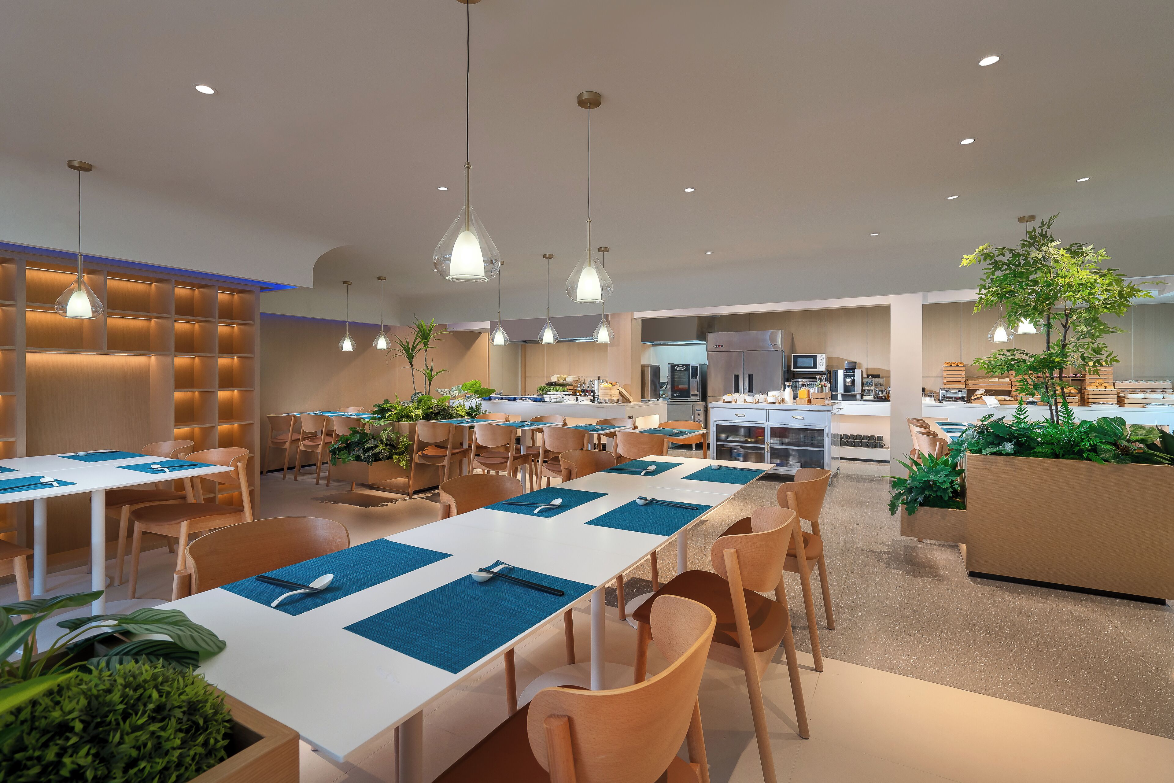 A modern dining area with white tables and blue placemats, surrounded by wooden chairs.