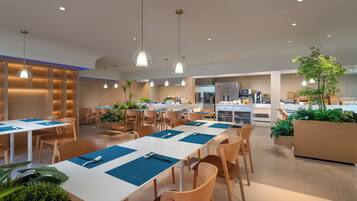 A modern dining area with white tables and blue placemats, surrounded by wooden chairs.