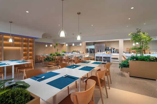 A modern dining area with white tables and blue placemats, surrounded by wooden chairs.