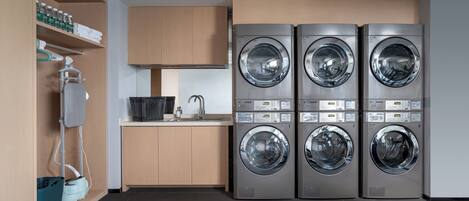 A modern laundry room with four stacked front-loading washing machines, a drying machine, a sink, and a drying rack.