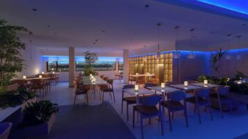 Um restaurante moderno com mesas e cadeiras dispostas em um espaço amplo, com iluminação ambiente e plantas em vasos.