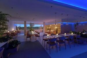 A modern restaurant with tables and chairs arranged in an open layout, featuring ambient lighting and potted plants.