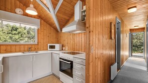 Una cocina moderna con paredes de madera, armarios blancos, un microondas y un ventanal con vistas a zonas verdes.