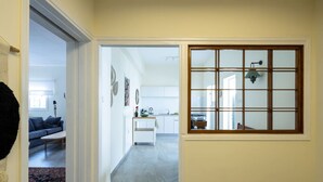 A hallway leading to a living room with a sofa and a coffee table, a kitchen area with cabinets and a sink, and a window with a grid pattern. - Eclectic Rabin Square Apt by Sea N' Rent (Tel Aviv)