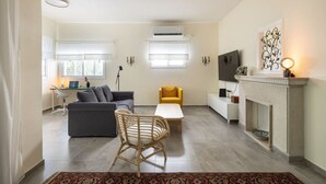 A modern living room with a grey sofa, a yellow armchair, a wicker chair, a small white table, and a fireplace. - Eclectic Rabin Square Apt by Sea N' Rent (Tel Aviv)