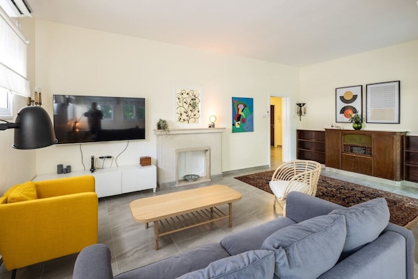 A modern living room with a sofa, a yellow chair, a wooden bench, a fireplace, and a TV mounted on the wall.