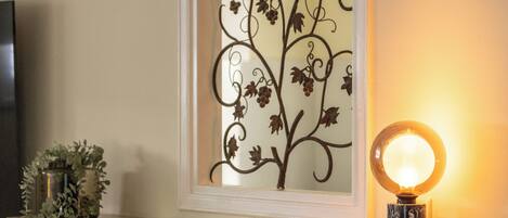 Un diseño de planta de metal decorativo en una pared, una lámpara redonda con espejo y una pequeña planta en maceta sobre una repisa.