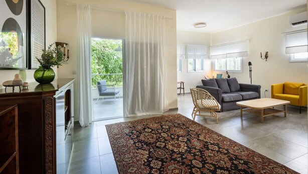 A spacious living room with a large rug, a sofa, a yellow armchair, and a dining table. - Eclectic Rabin Square Apt by Sea N' Rent (Tel Aviv)