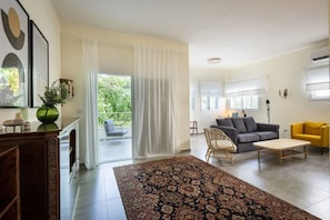 A living room with a sofa, a yellow armchair, a coffee table, a patterned rug, a wicker chair, and a view of the outdoors.