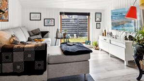 A modern living room with a sofa, a coffee table, and a TV. There is a window with a view of the outside.