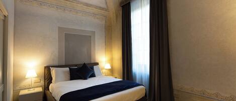 A hotel room with a large bed, two bedside lamps, a nightstand, and a window with curtains.