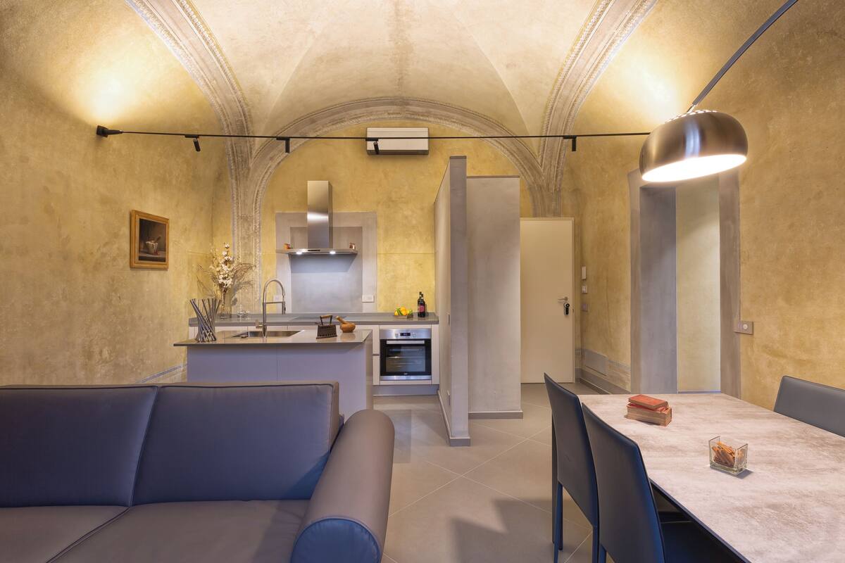 A modern kitchen with a central island, built-in oven, and a dining area with a table and chairs.