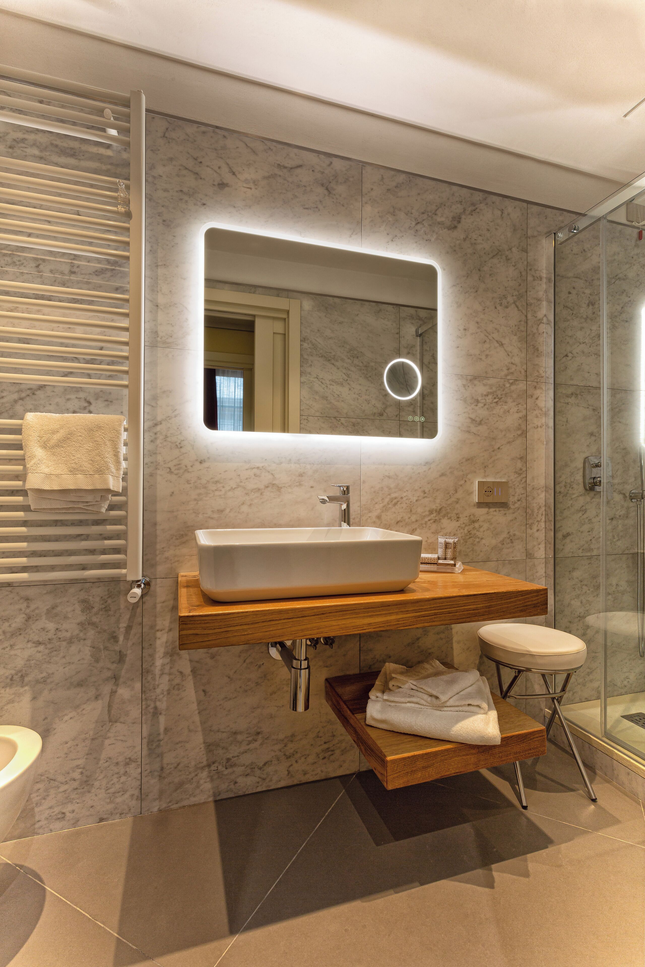 A modern bathroom with a large mirror, a vessel sink, a wooden vanity, a glass shower enclosure, and a towel rack.