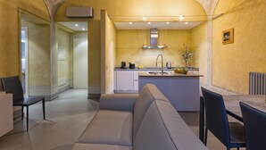 A modern kitchen with a built-in island, a dining area with a gray sofa, and a view of the adjacent living room. - Casa del Sarto (Florence)