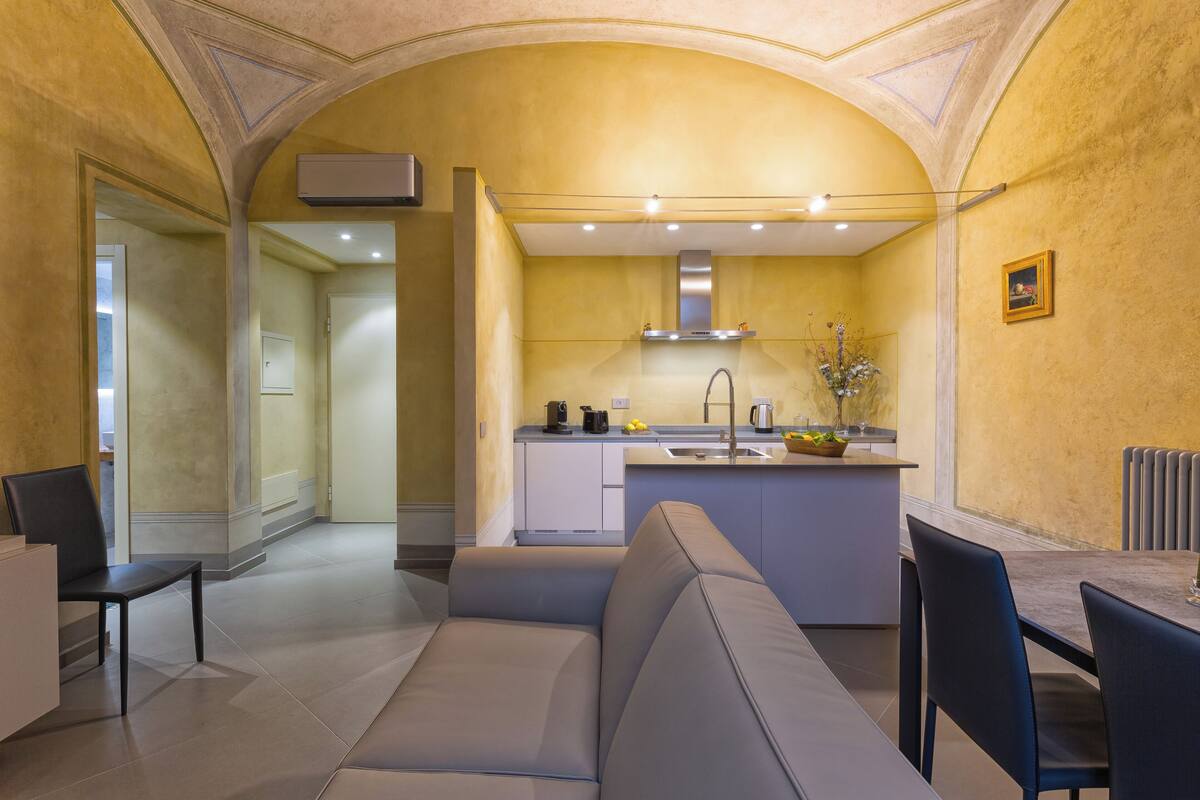 A modern kitchen with a built-in island, a dining area with a gray sofa, and a view of the adjacent living room.