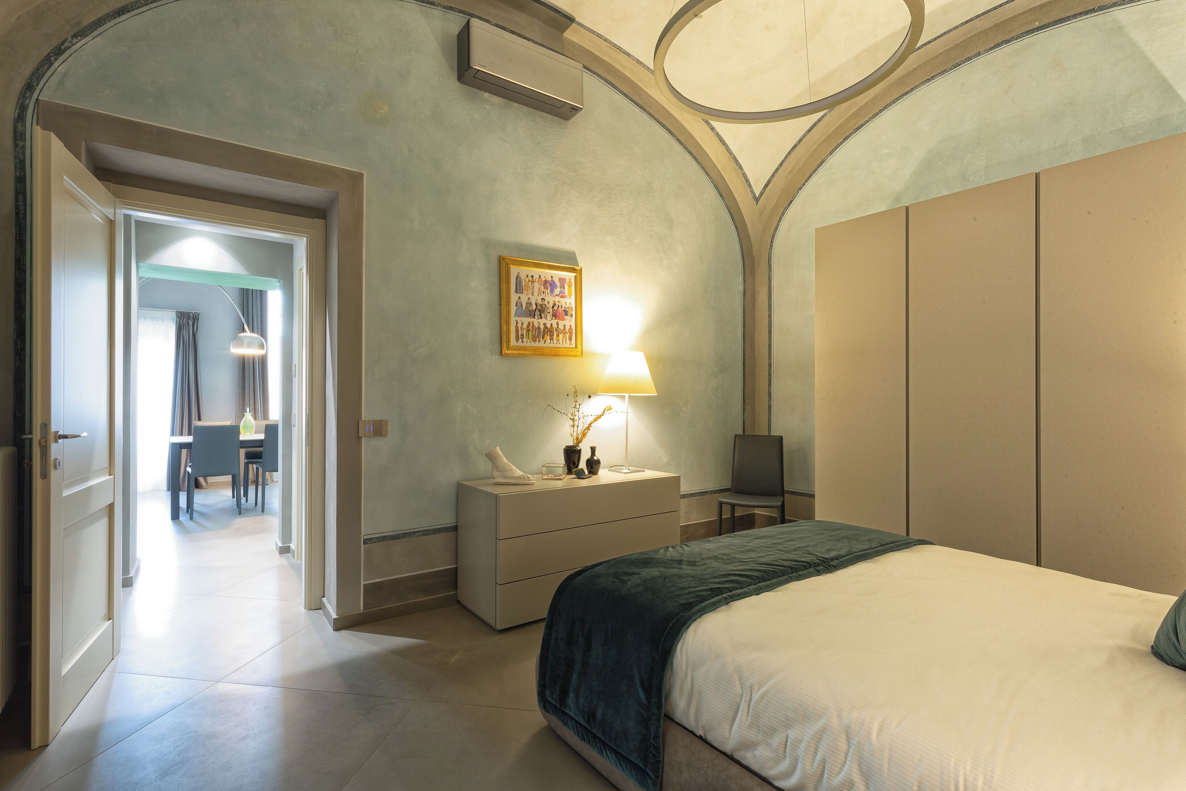 A bedroom with a bed, a nightstand, a lamp, a framed picture, and a wardrobe.