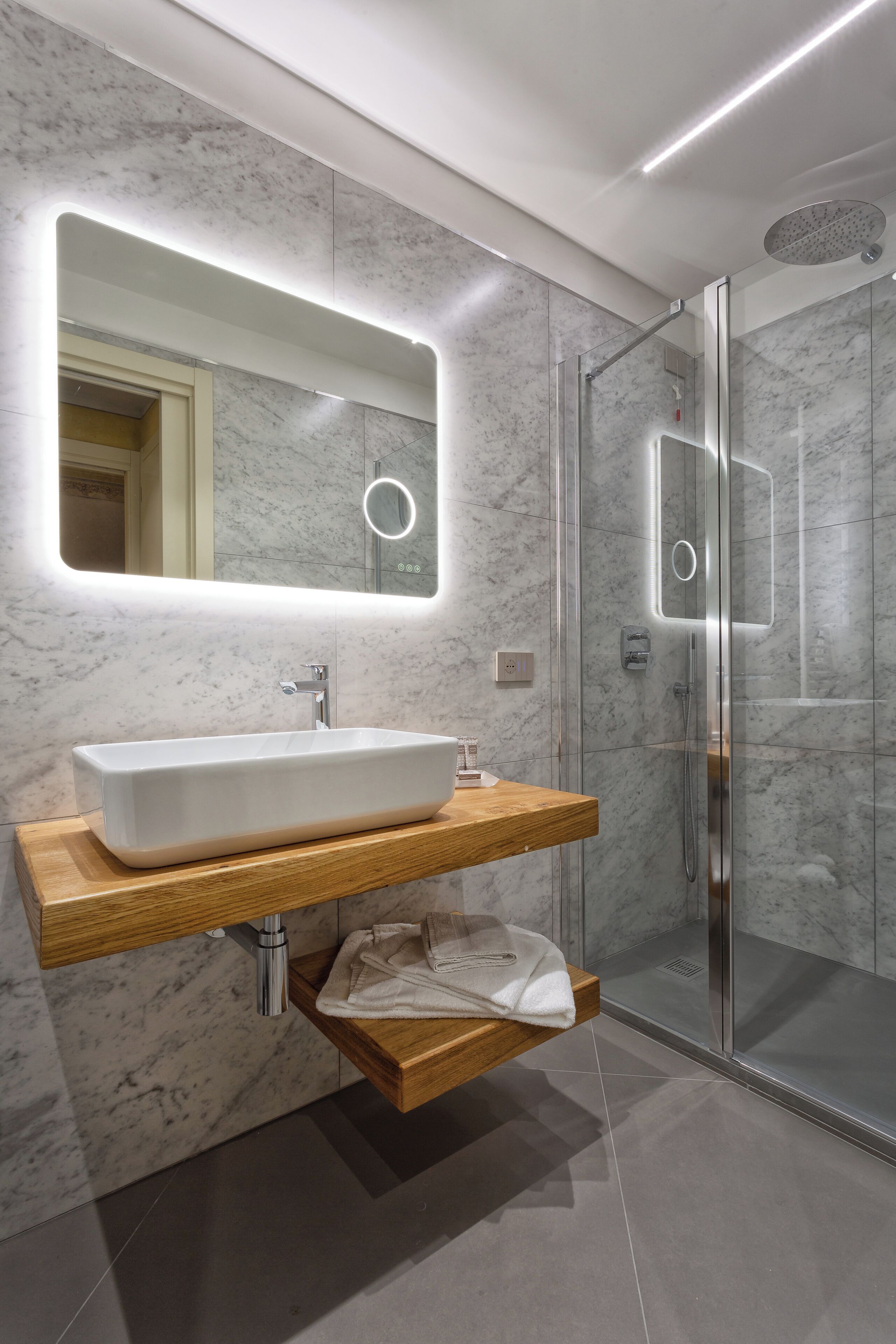 Een moderne badkamer met een rechthoekig wastafelmeubel, een houten kast en marmeren wanden, plus een douchecabine met glazen wanden.
