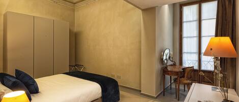 A hotel room with a bed, bedside lamps, a desk with a chair, and a window with curtains.