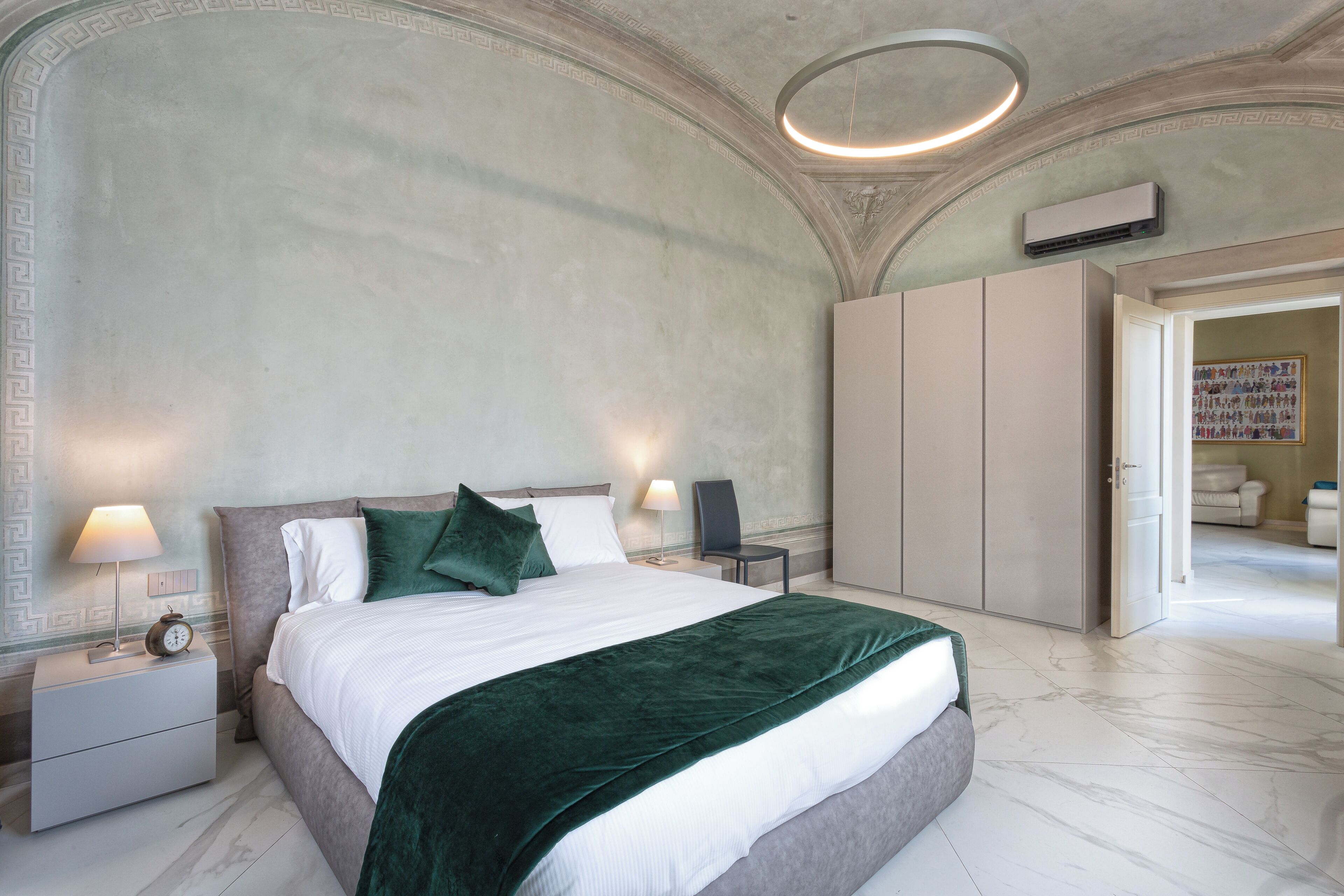 Un dormitorio moderno con una cama grande, una mesita de noche con lámpara, un armario y una puerta que da a otra habitación.