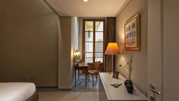 Ein Hotelzimmer mit Bett, Schreibtisch mit Lampe, Stuhl und einer Vase mit Blumen.