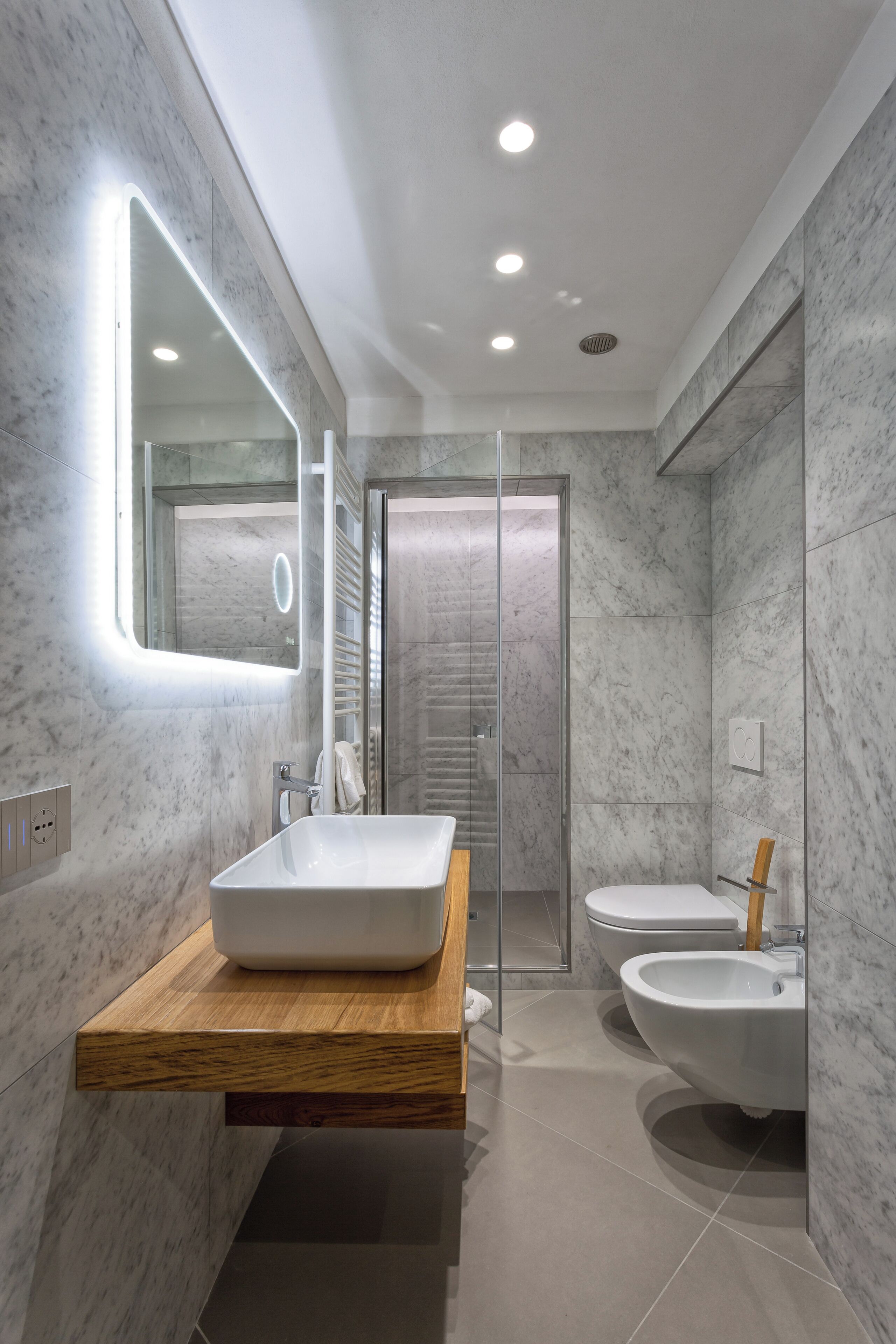 Un baño moderno con un espejo grande, un tocador de madera, un bidé y una cabina de ducha de vidrio.