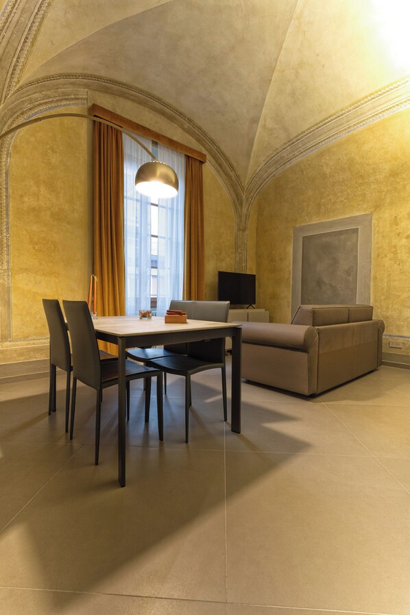 A dining area with a table and chairs, a sofa, a TV, and a large window with curtains.