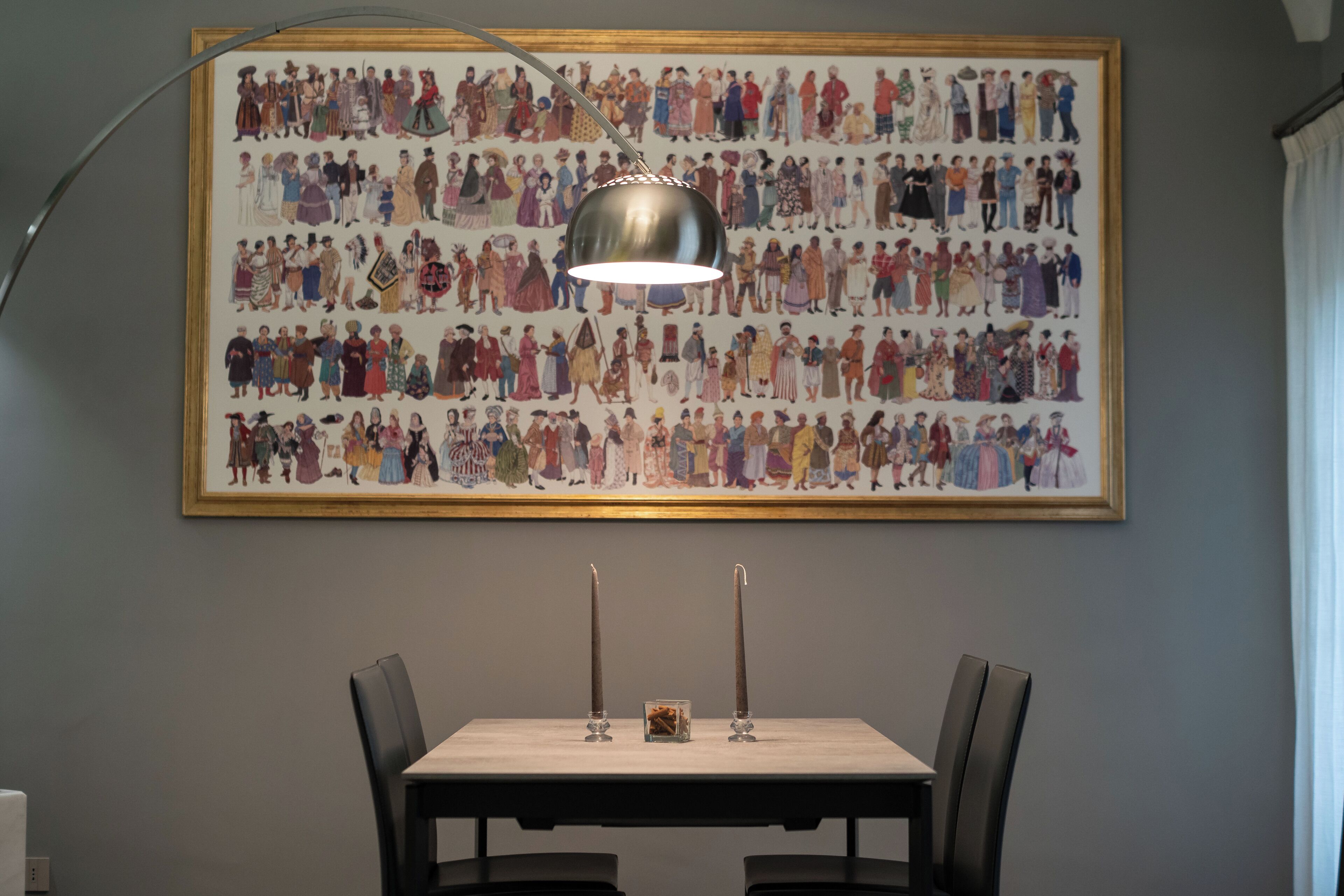 A dining area with a table, chairs, a pendant light, and a large illustrated wall art.