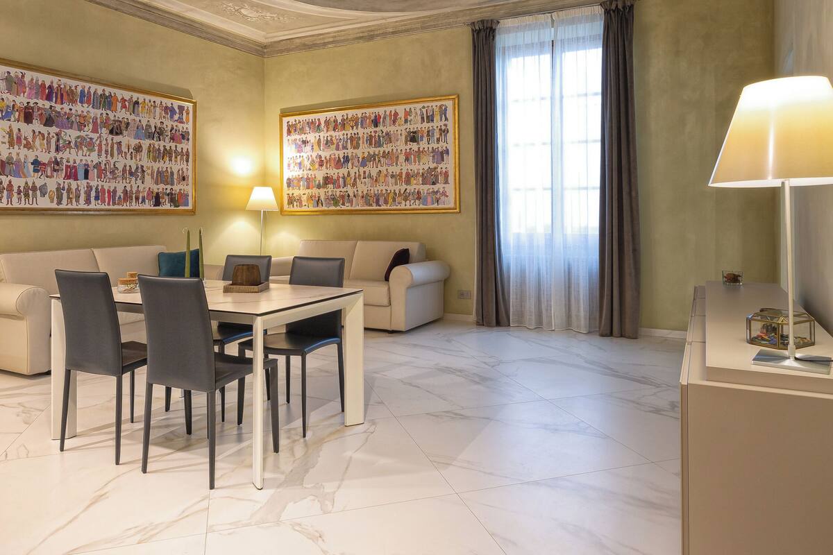 A spacious room with a marble floor, a dining table with chairs, a sofa, and a lamp.
