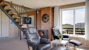 Una sala de estar acogedora con chimenea, sillones de cuero, televisor y un amplio ventanal con vistas panorámicas.