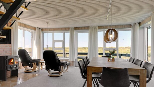 Amplia habitación con una gran mesa de madera, varias sillas, una chimenea y ventanas amplias con vistas al exterior.