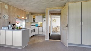 Una cocina compacta con armarios blancos, un microondas, una tetera y un reloj en la pared.