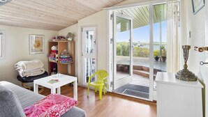Una habitación acogedora con techo de madera, una mesa blanca, una silla amarilla y un gran ventanal corredero que da a un espacio al aire libre.